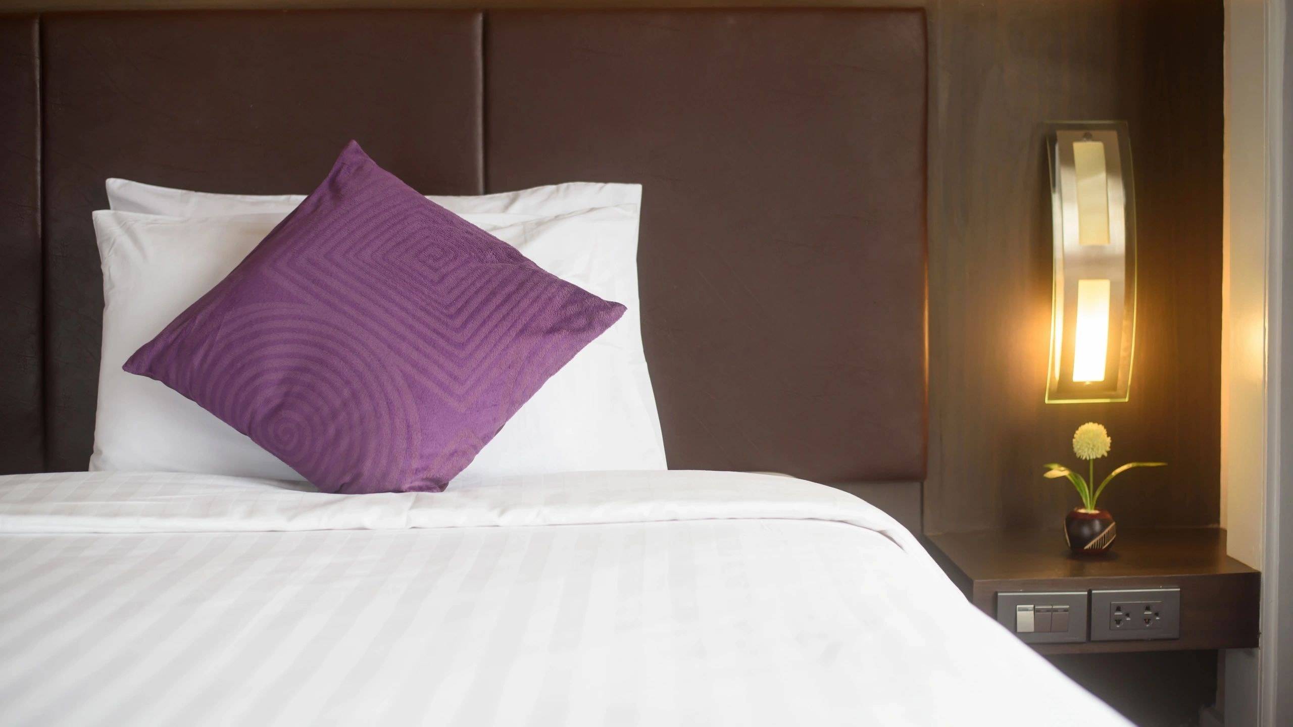 Hotel bedroom with purple pillow and white linens